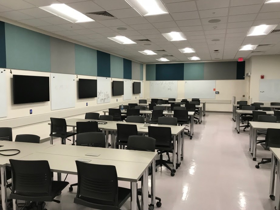 classroom with desks and chairs on wheels, white boards, large tv screens