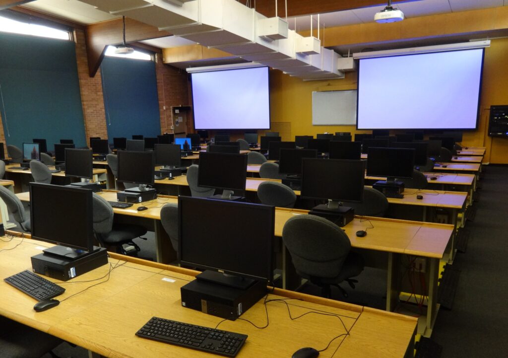 many computers on desks with chairs