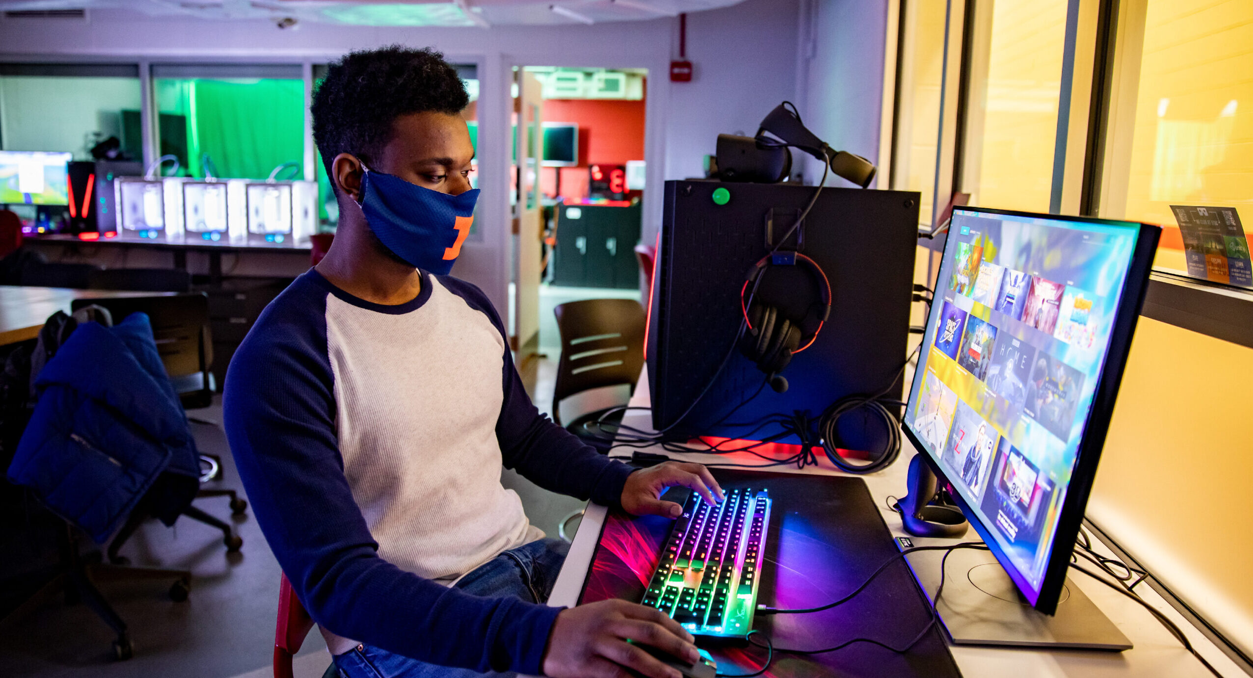 student wearing a mask issitting in chair using two computer monitors with mouse and keyboard